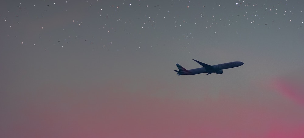 Plane flying past pink sunset