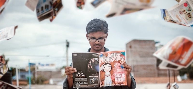 Magazine pages swirl around a person reading