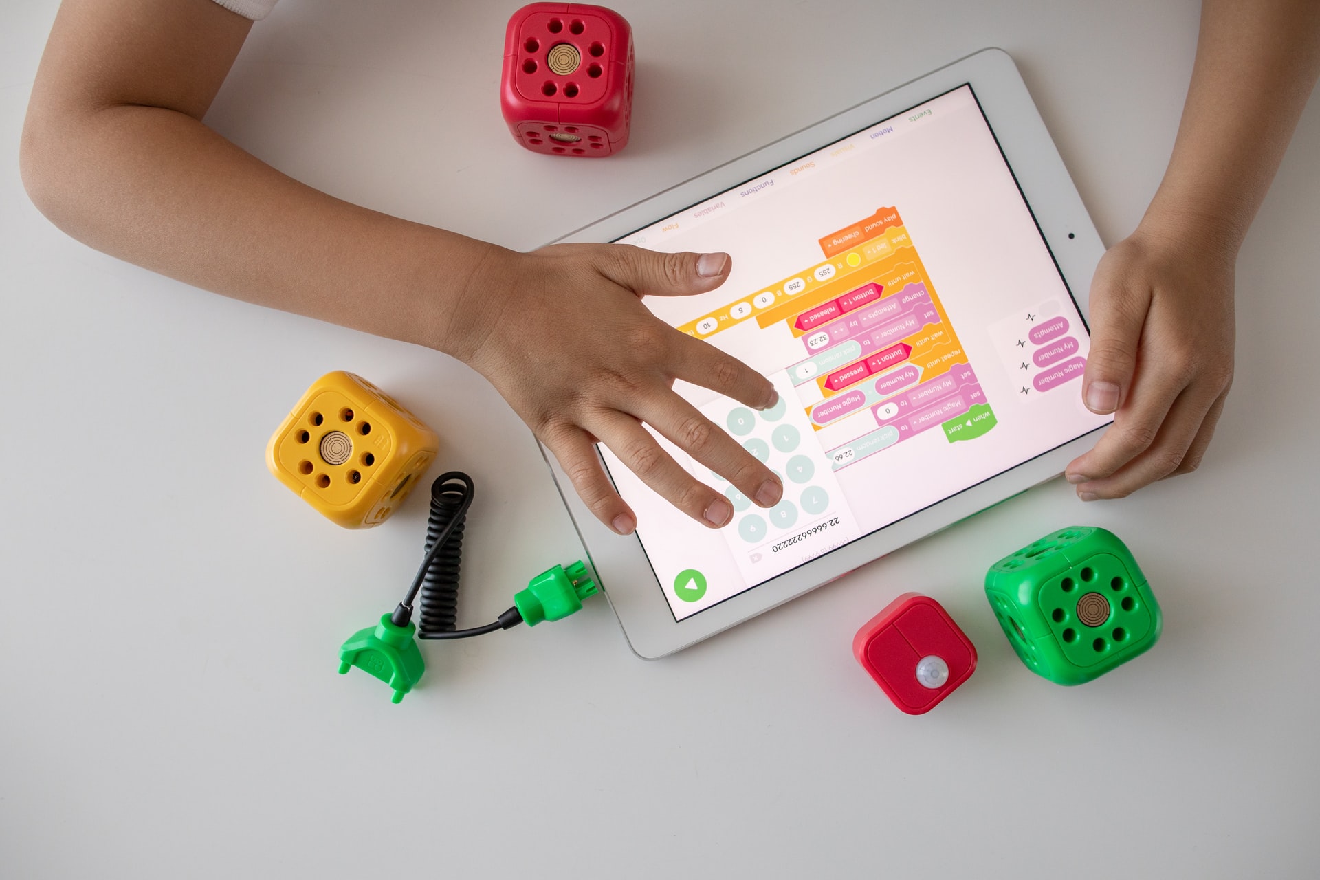 small hands on an white tablet navigating a mobile app with brightly colored toys and blocks on a white table