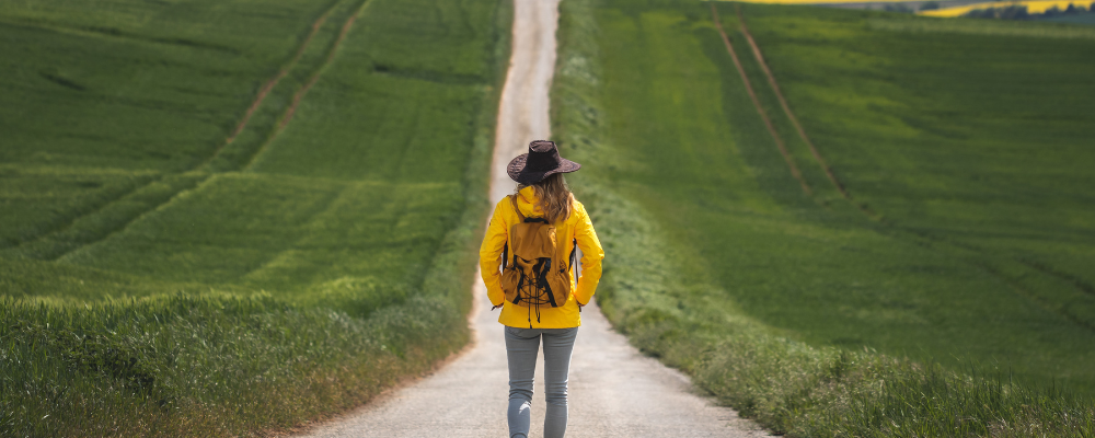 the stitchology story person in yellow coat on a path surrounded by green grass